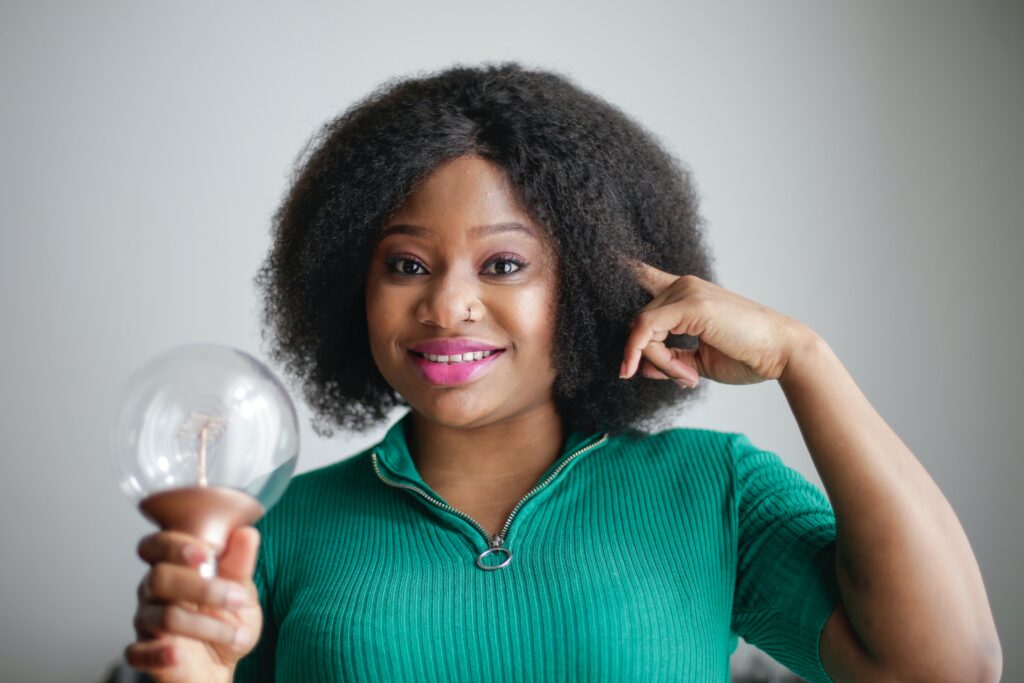 A women showing the power of creative thinking exercises by holding a light bulb on her hand and pointing finger to her head