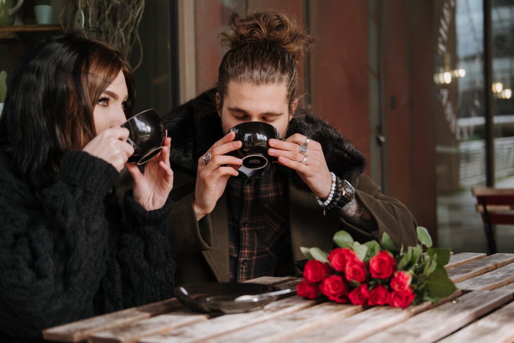 A couple having coffee at a café with a bunch of red roses on the table