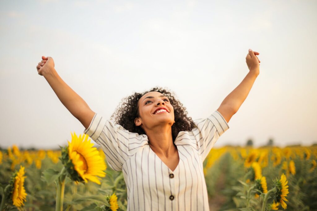 A girl standing on a sunflower field while raising both hands on top 