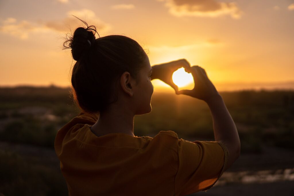 A girl doing hand heart sign during the sunset