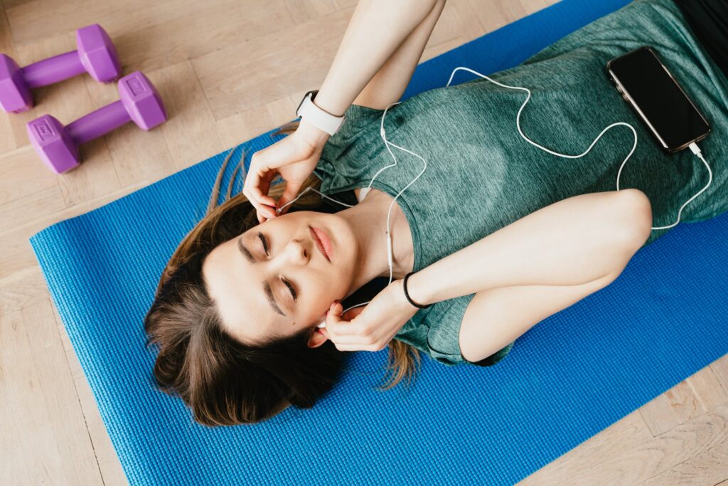 a girl laying on a mat and listing to music through earphone as one of her stress relief routines