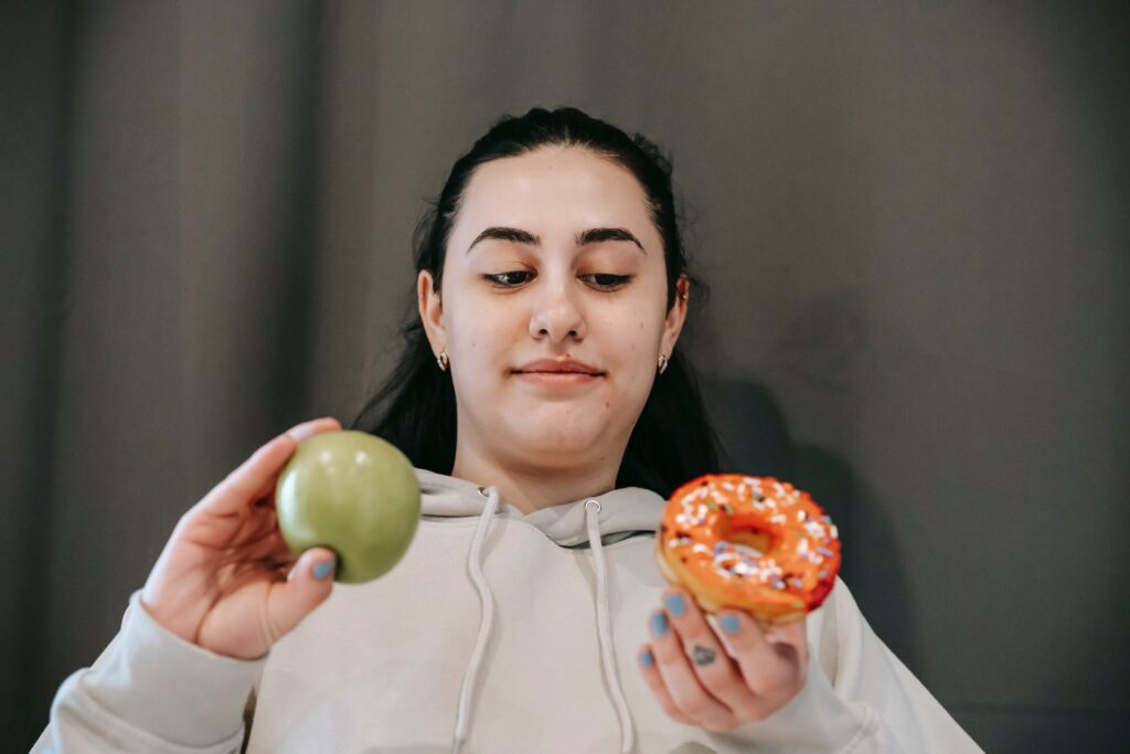 A girl with a green apple on one hand and a donut on other hand