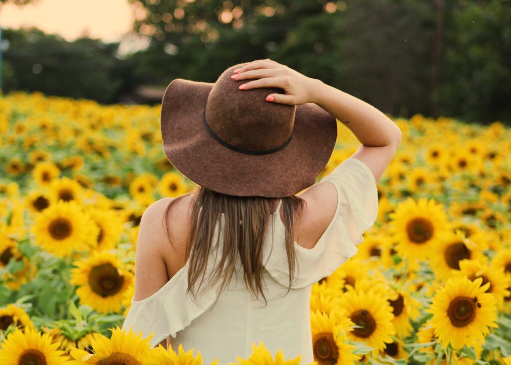 A lady touching her hat in a sunflower field