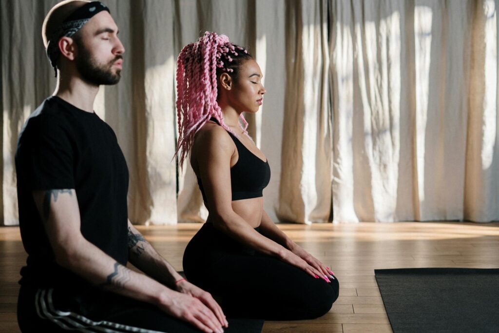 A woman and a man in black outfit practicing meditation to boost yoga motivation