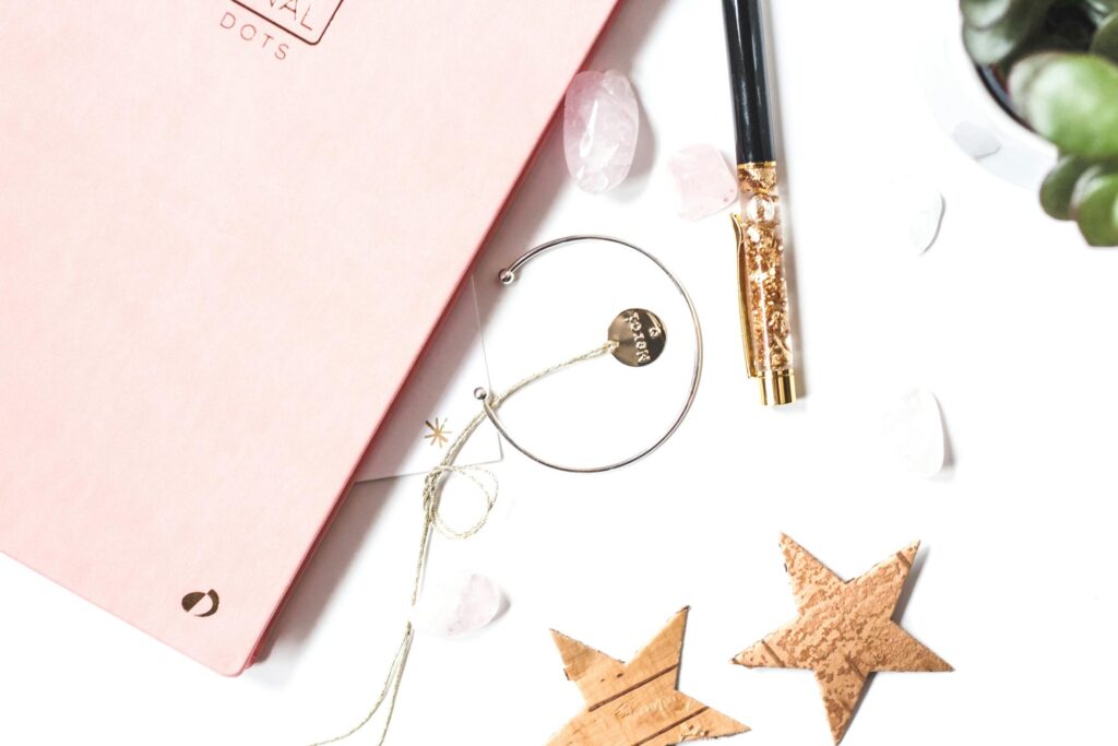 A close up picture of a notebook beside a silver color bracelet, stars and a pen