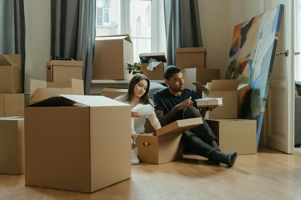 A man and a woman unboxing cardboard boxes sitting on the floor 